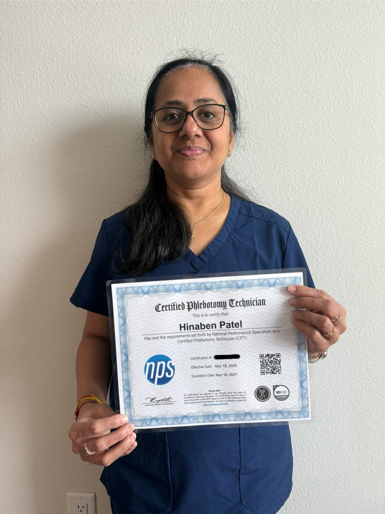 VMI graduate Hinaben Patel in navy scrubs holding her Certified Phlebotomy Technician certificate